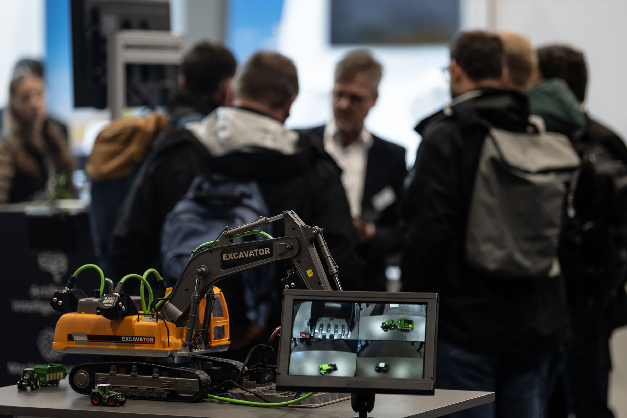 Trade fair situation: tractor model with cameras in the foreground, visitors chatting in the background